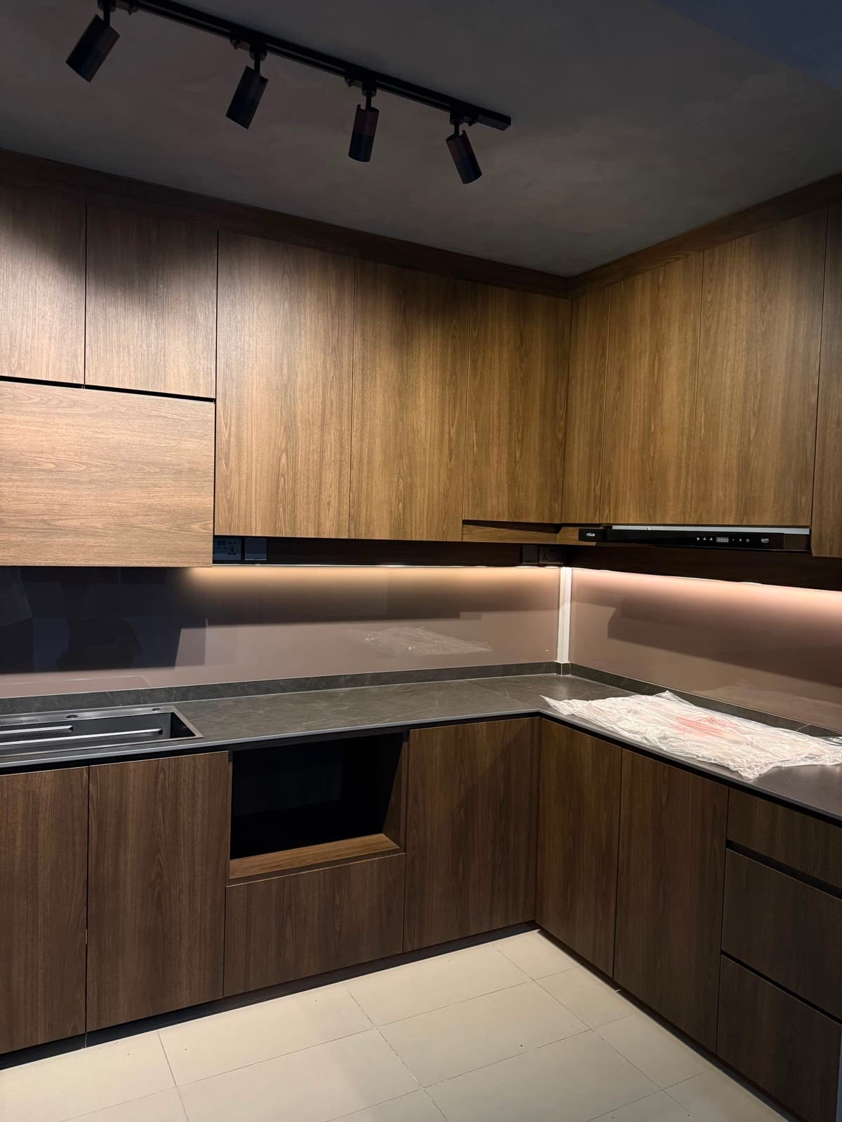 Complete kitchen wrapped in warm walnut wood-grain with cove lighting